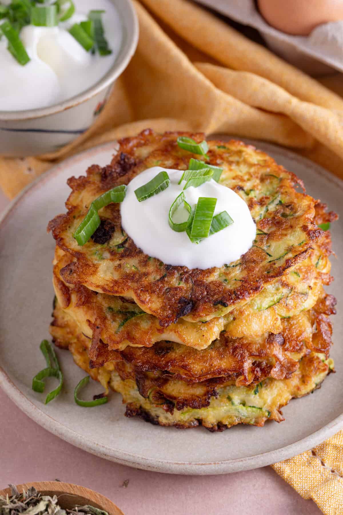 A plate of courgette and halloumi fritters stacked up with garlic yoghurt on top.