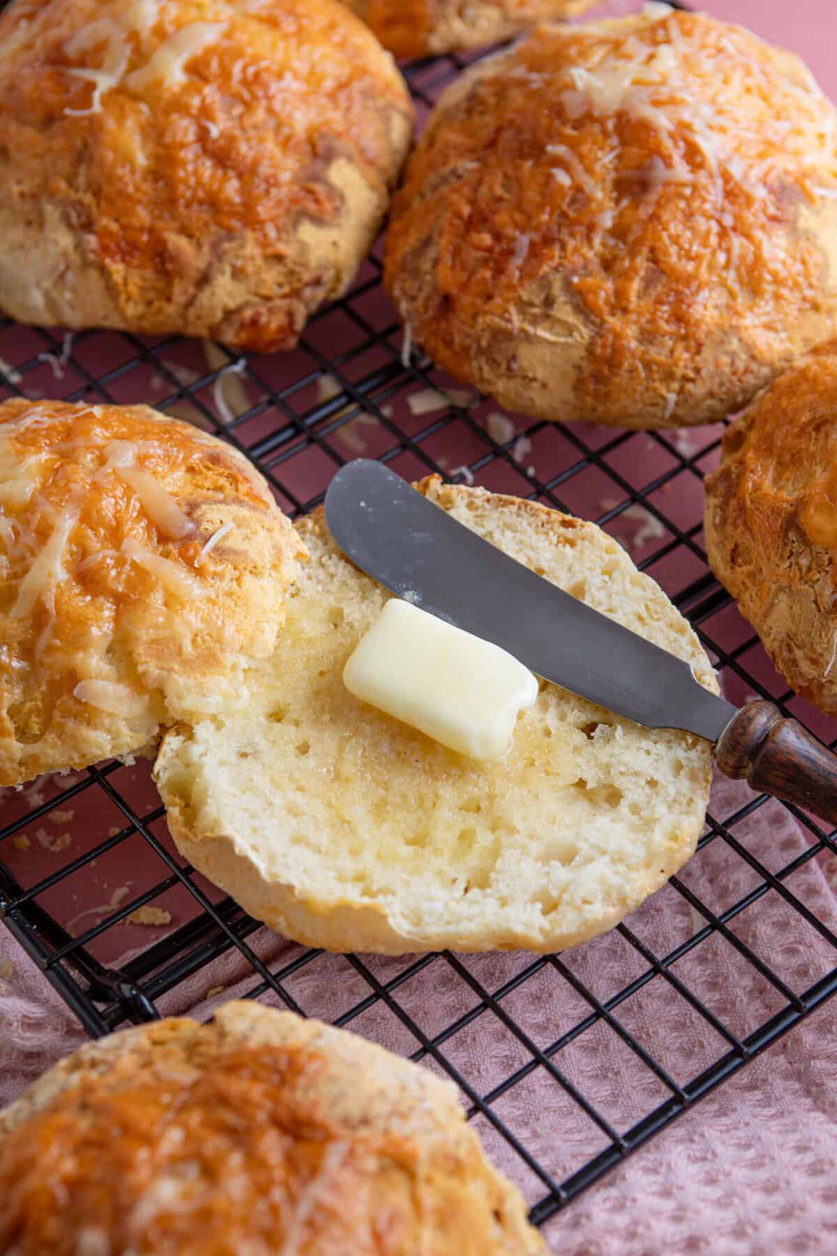 A gluten free cheesy bread roll cut in half with butter on.