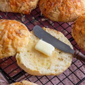 A gluten free cheesy bread roll cut in half with butter on.