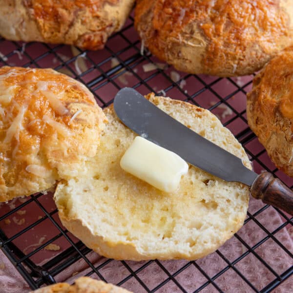A gluten free cheesy bread roll cut in half with butter on.