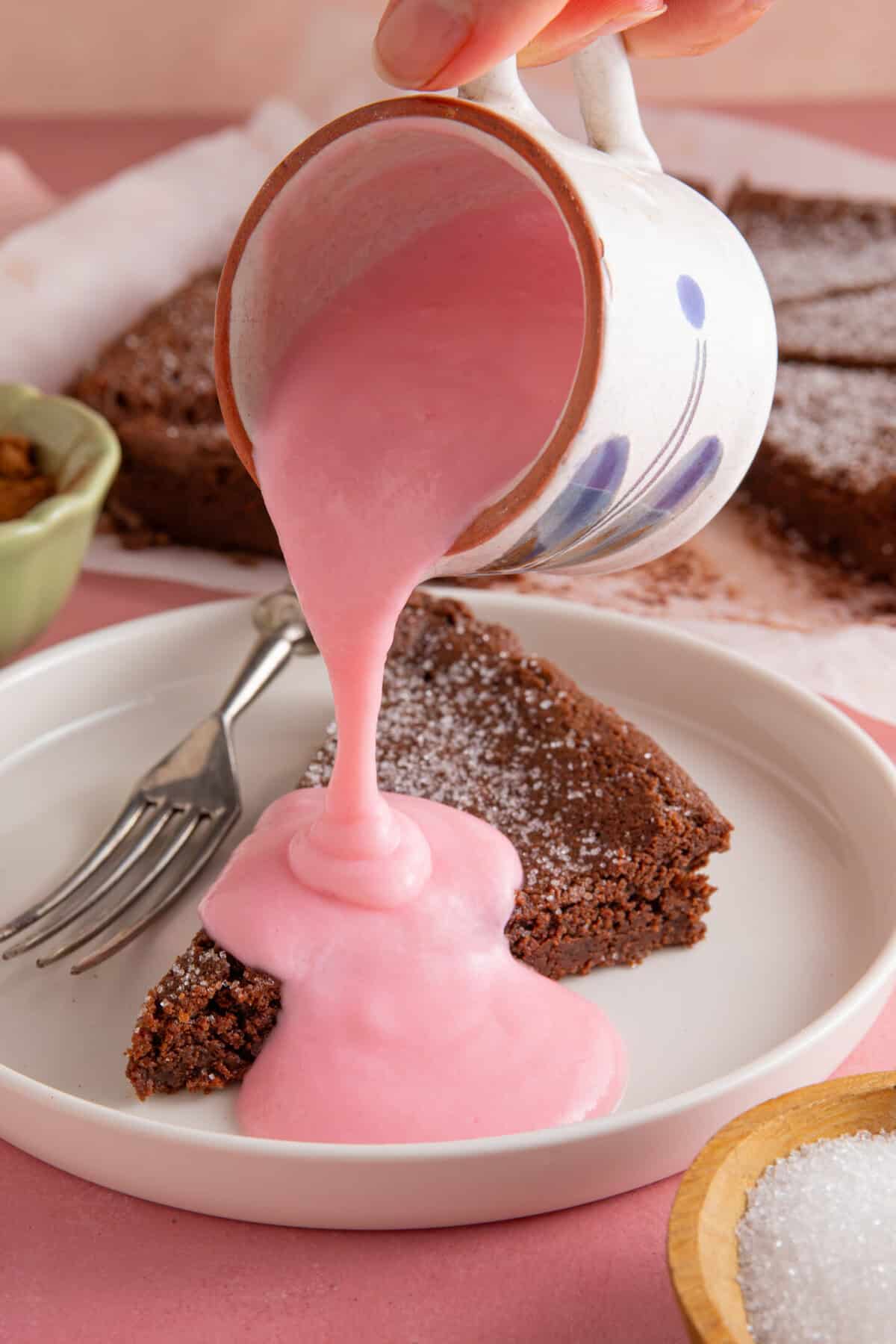 A jug of pink custard pouring over a slice of chocolate concrete.