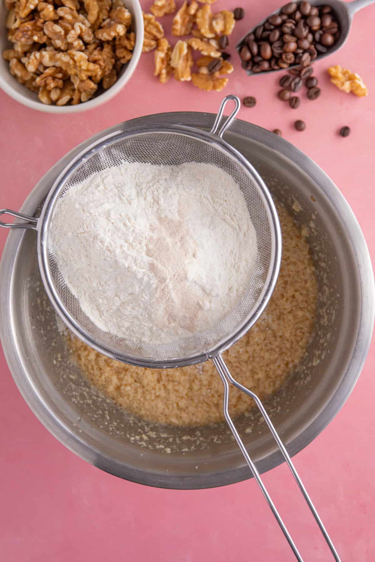 Process shot for gluten free coffee and walnut cake showing the dry ingredients being sieved into the batter.