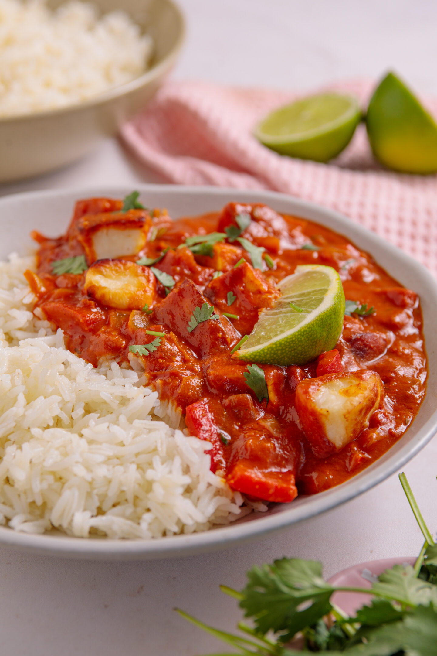 A bowl of halloumi curry with rice and lime wedges on top.