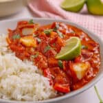 A bowl of halloumi curry with rice and lime wedges on top.