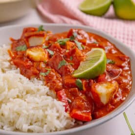 A bowl of halloumi curry with rice and lime wedges on top.