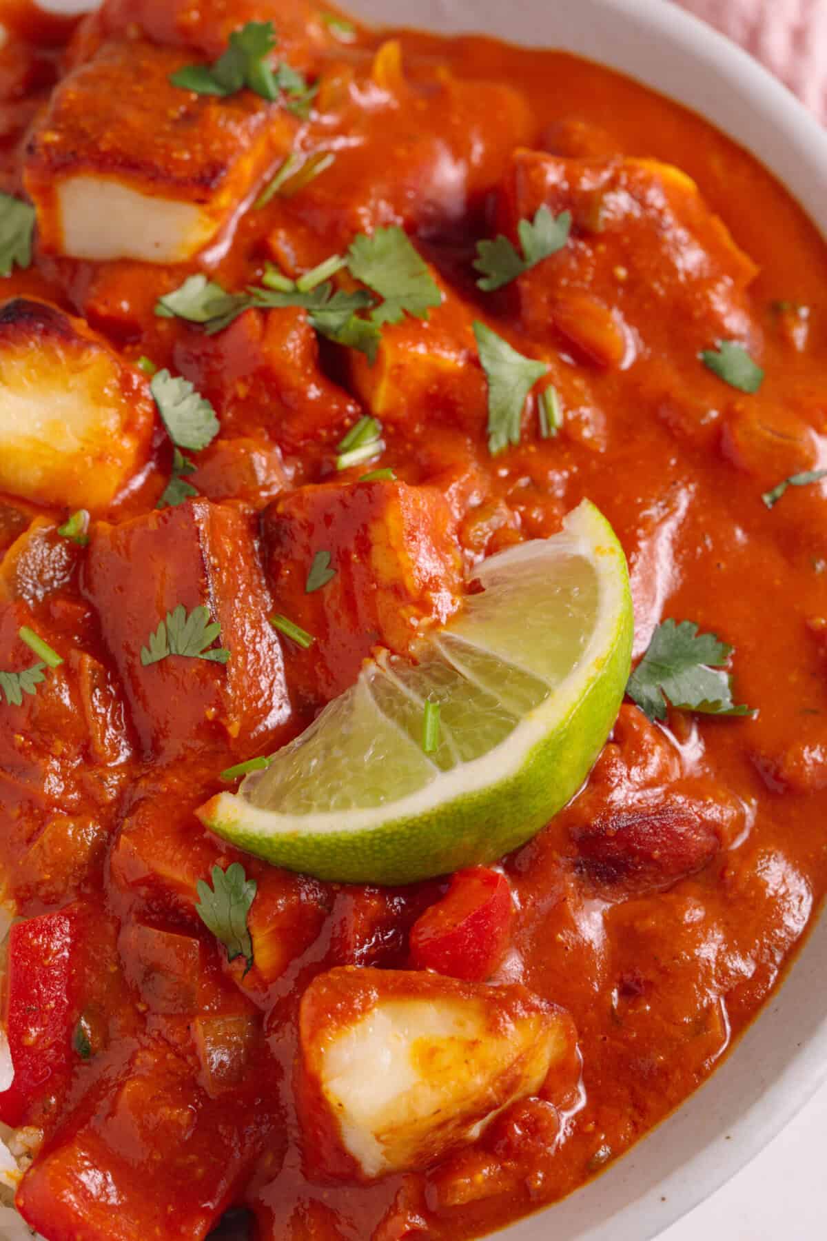 Close up shot of a halloumi curry with coriander, crispy halloumi chunks and a lime wedge on top.