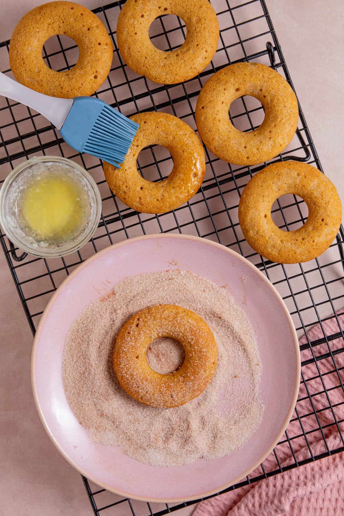 Process shots for gluten free pumpkin donuts recipe showing the baked donuts being coated in sugar.