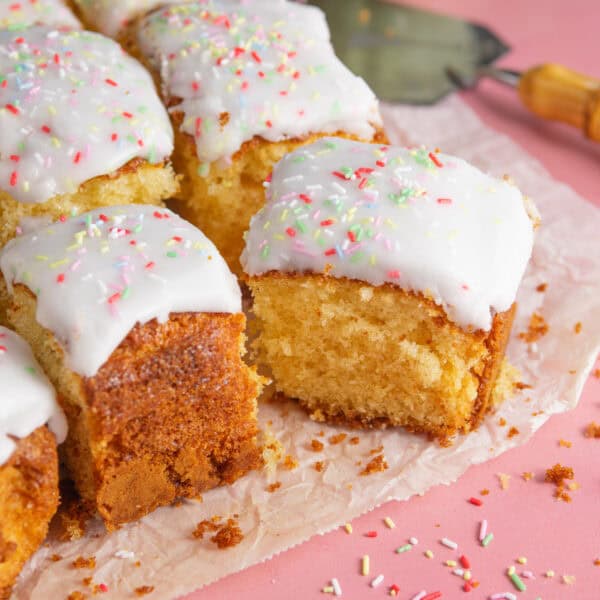 Squares of gluten free school dinner cake with thick white icing and rainbow sprinkles.