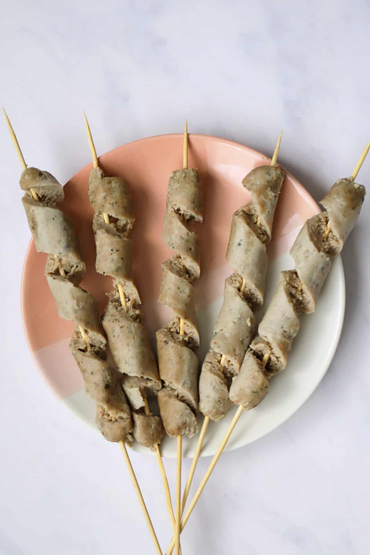 Process shot of gluten free turkey twizzlers showing a plate of boiled turkey sausages on wooden skewers, cut into spirals.