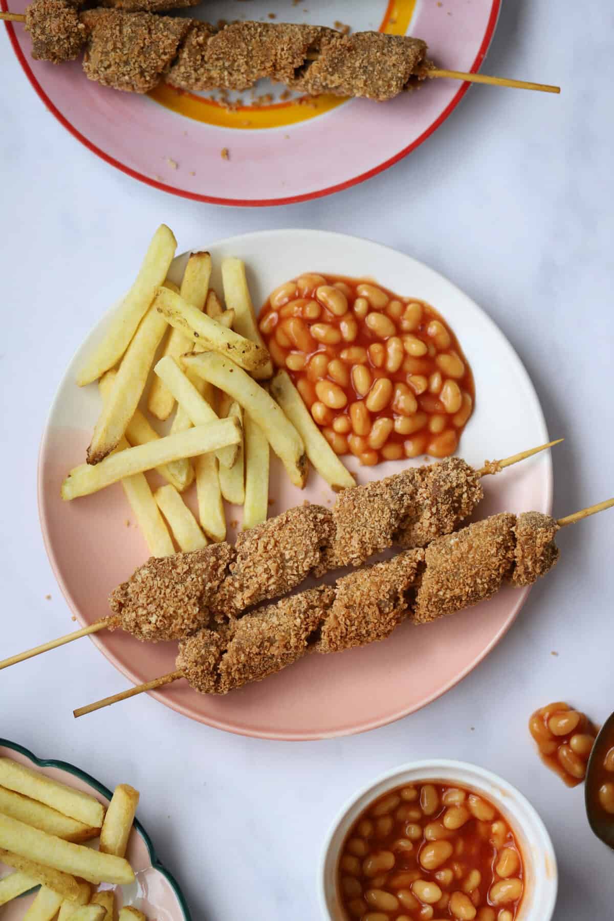 A plate with two turkey twizzlers, baked beans and fries.