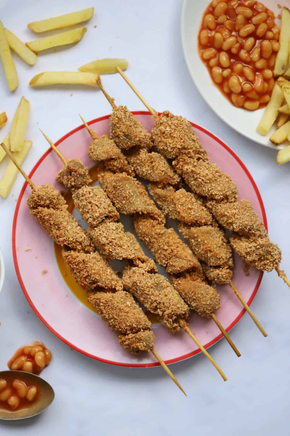 A plate of gluten free turkey twizzlers with chips and beans on the side.