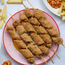 A plate of gluten free turkey twizzlers with chips and beans on the side.