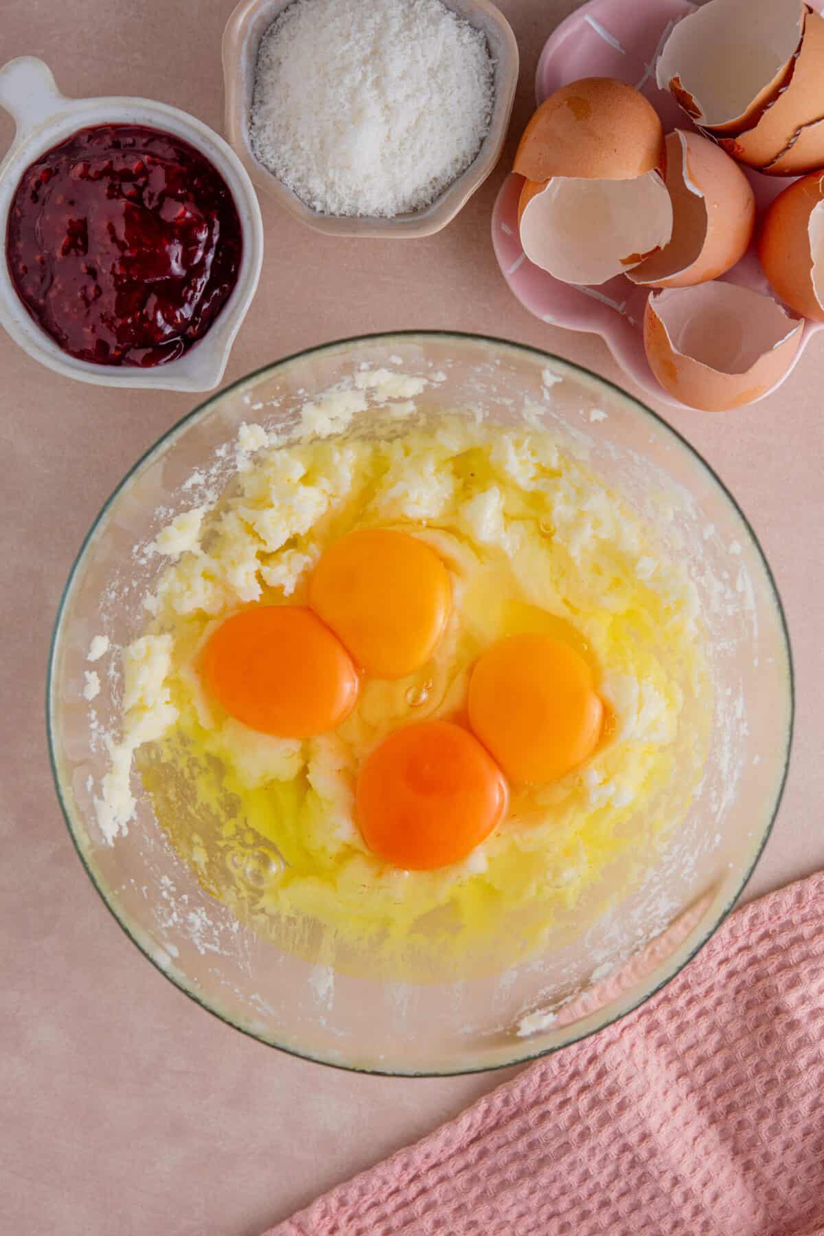 Process shot of jam and coconut sponge showing the eggs added to the cake mixture.
