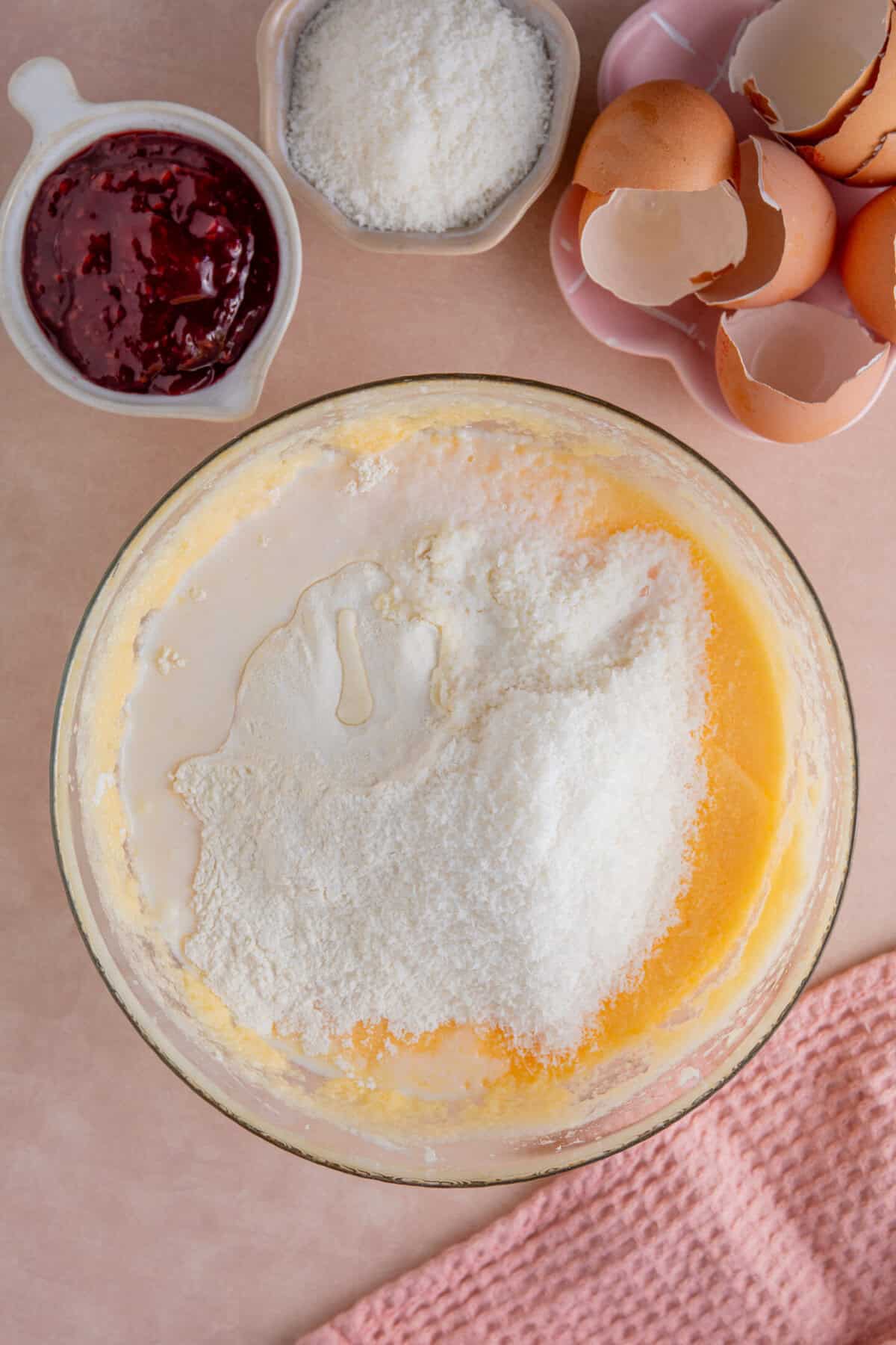 Process shot of jam and coconut sponge showing the flour and coconut added to the wet mixture.