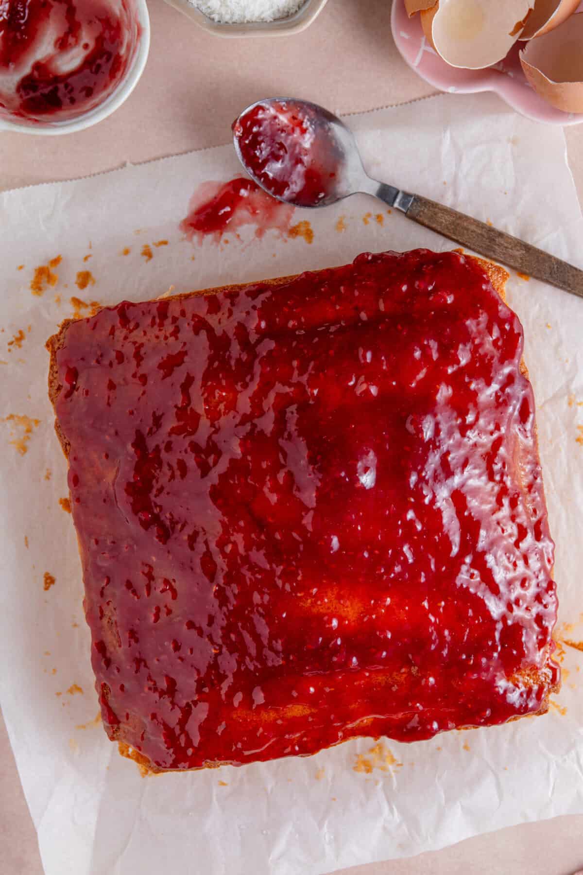 Process shot of jam and coconut sponge showing the cake spread with jam.