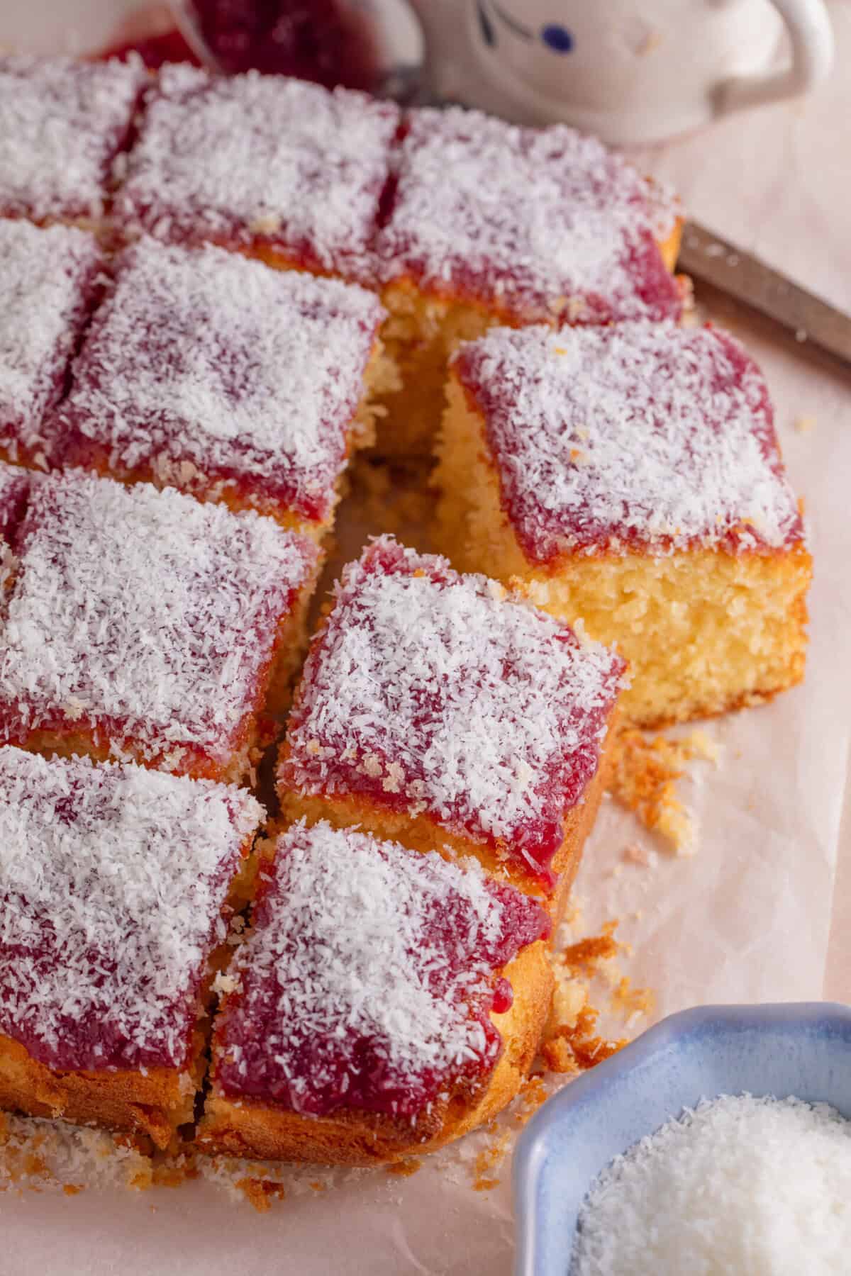 A gluten free jam and coconut sponge cake cut into squares.