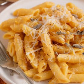 Close up of a bowl of creamy pumpkin pasta with parmesan and sage on top.