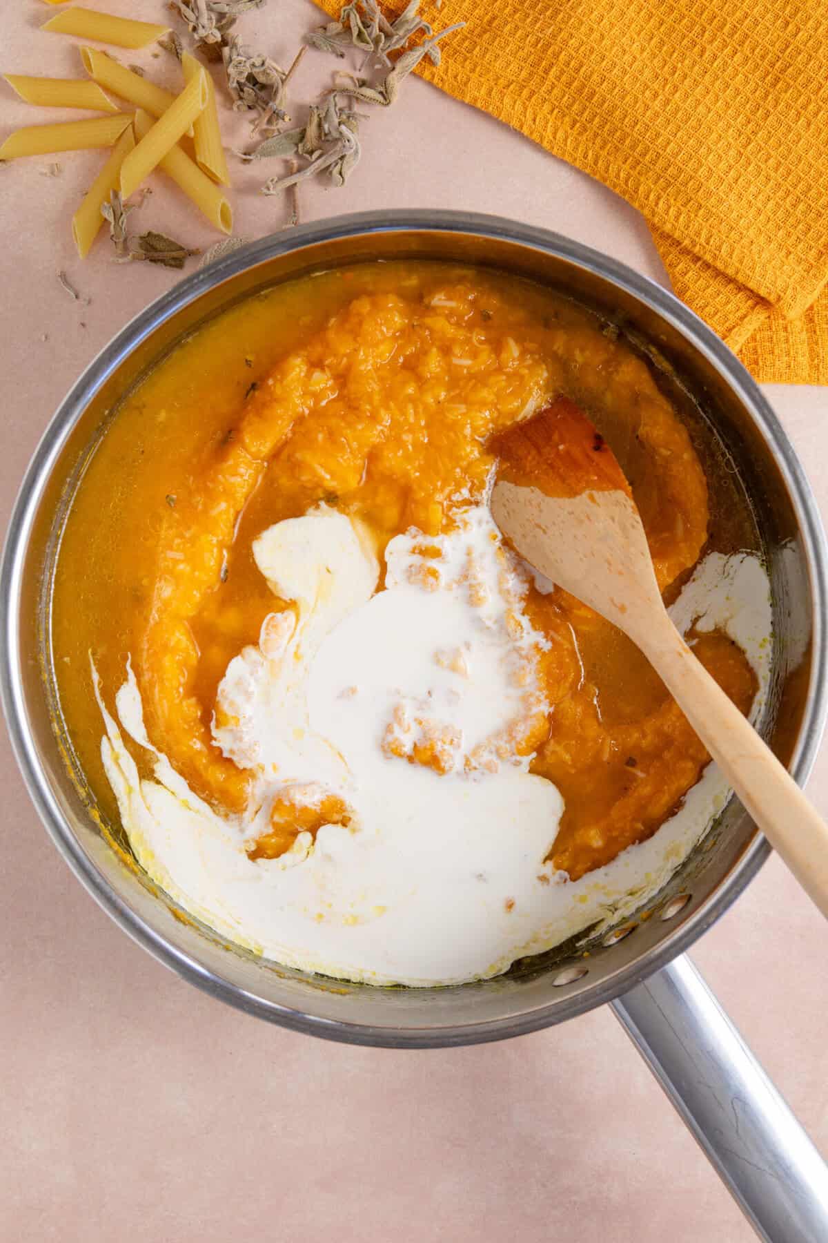 Creamy pumpkin pasta sauce in a saucepan with a wooden spoon.