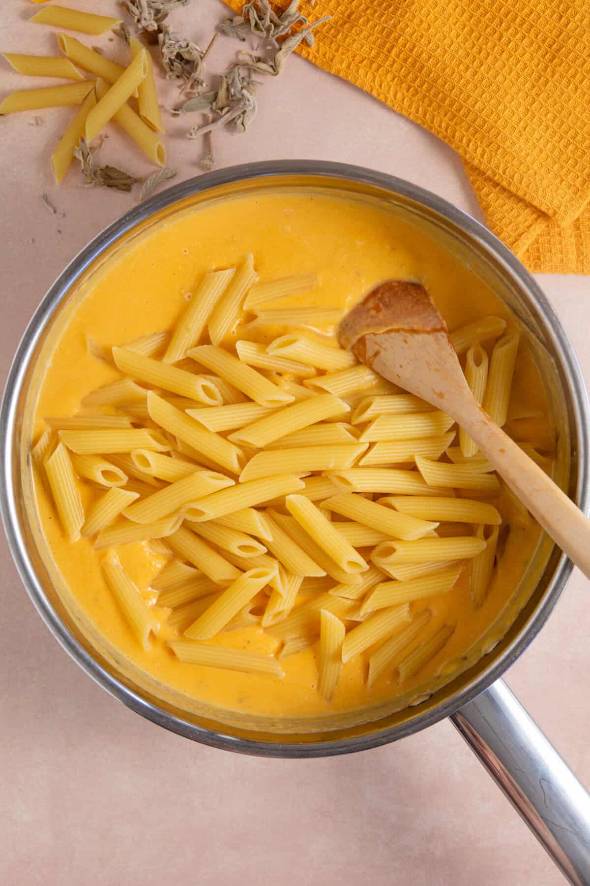 Process shot for creamy pumpkin pasta showing the drained pasta added to the pumpkin sauce in a pan.