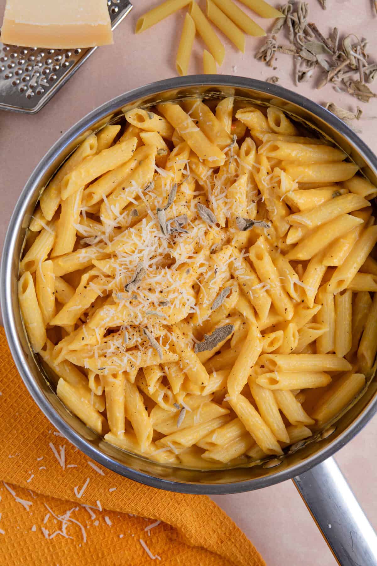 A pan of creamy pumkin pasta with sage and parmesan on top.
