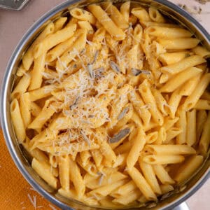 A pan of creamy pumkin pasta with sage and parmesan on top.