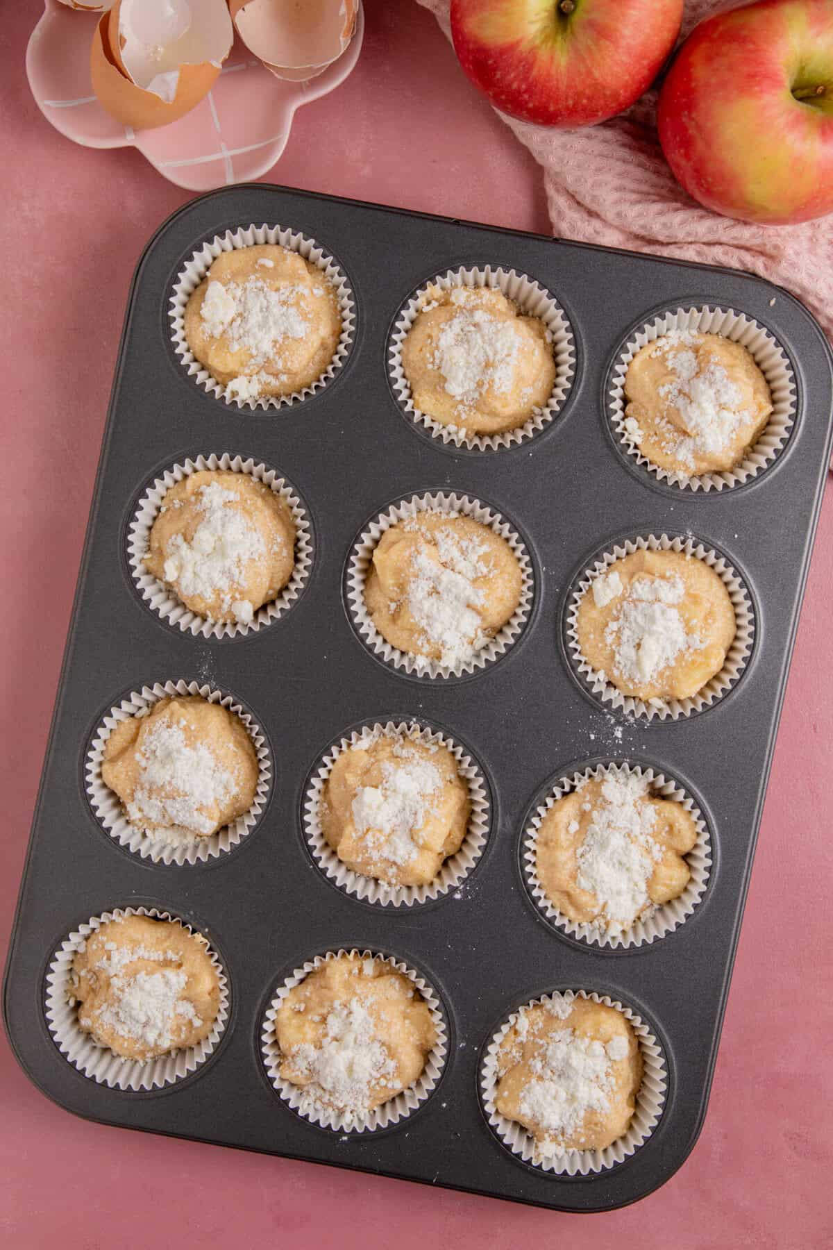 Process shot of gluten free apple crumble cupcakes showing the cake mixture divided between the cupcakes ready to bake.