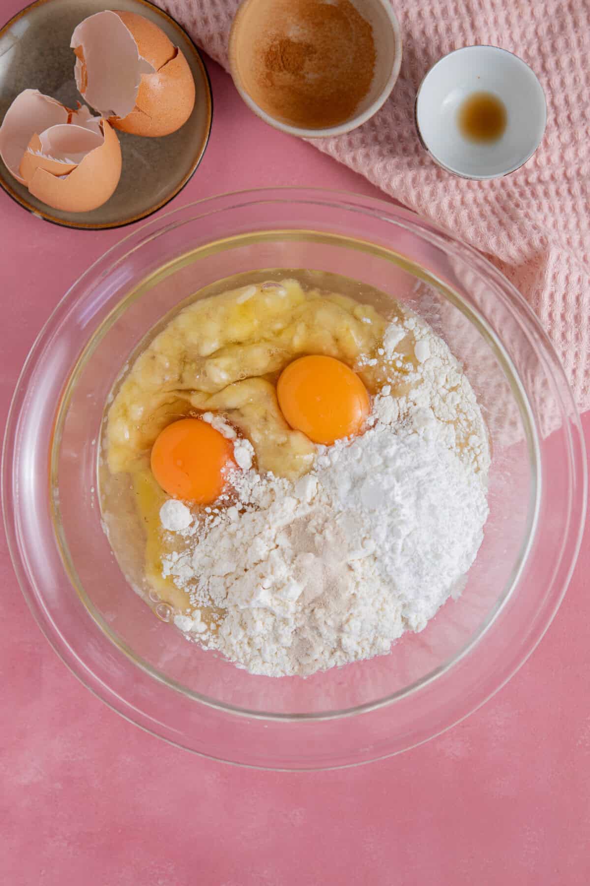 Process shot of cinnamon swirl banana bread showing the eggs, banana and flour in a mixing bowl.