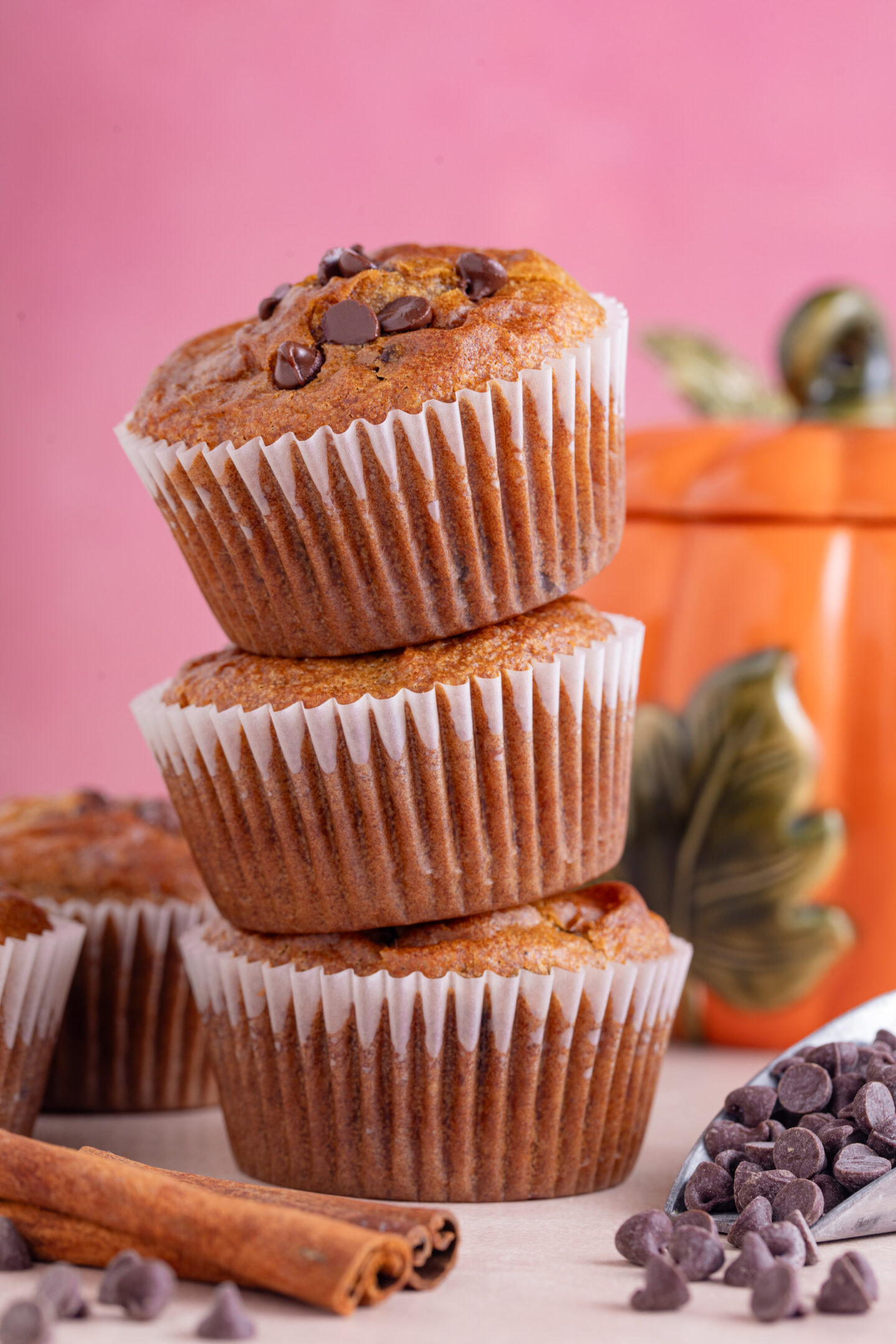 A stack of gluten free pumpkin chocolate chip mufffins with a pink background.
