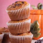 A stack of gluten free pumpkin chocolate chip mufffins with a pink background.
