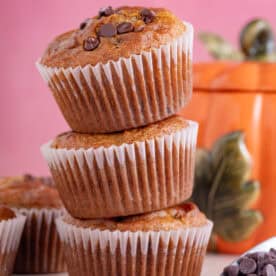 A stack of gluten free pumpkin chocolate chip mufffins with a pink background.