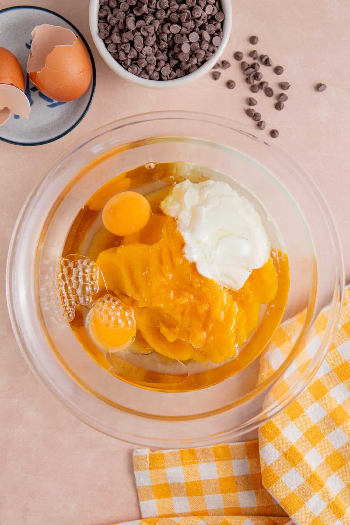 Process shot for gluten free pumpkin chocolate chip muffins showing the eggs, yoghurt and pumpkin added to a bowl.