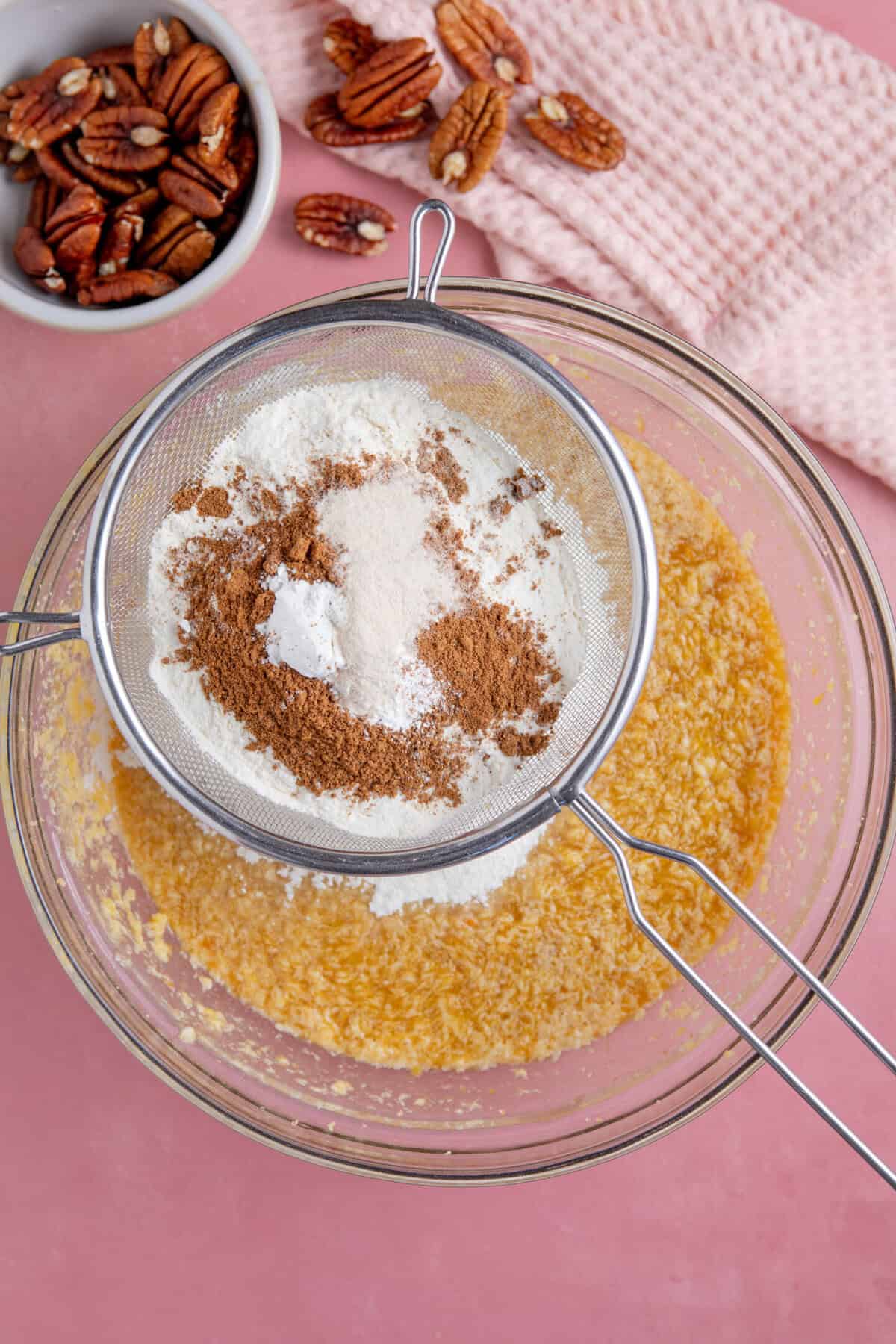 Process shot for a pumpkin spice latte cake showing the dry ingredients being sieved into the mixture.