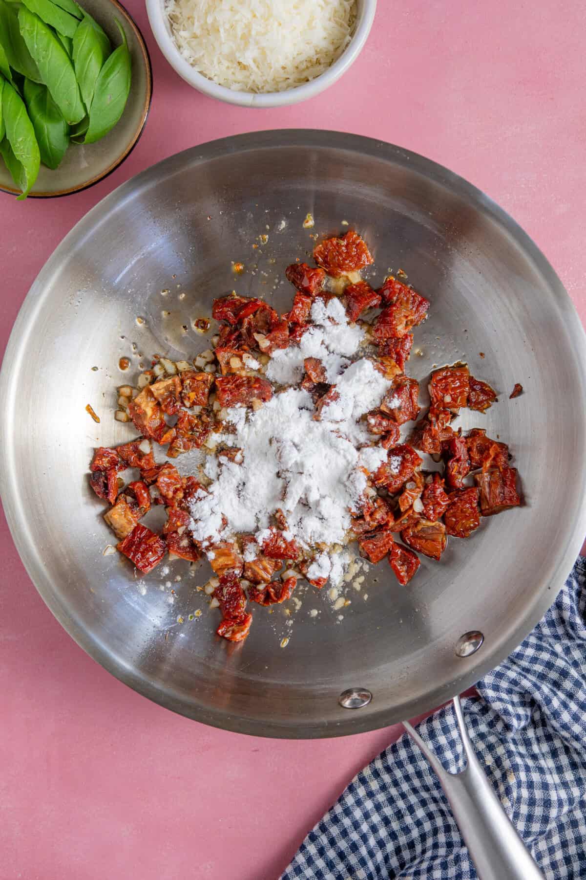 Process shot for Marry Me Chicken Meatballs showing the sun dried tomatoes, garlic, herbs and flour in a pan.