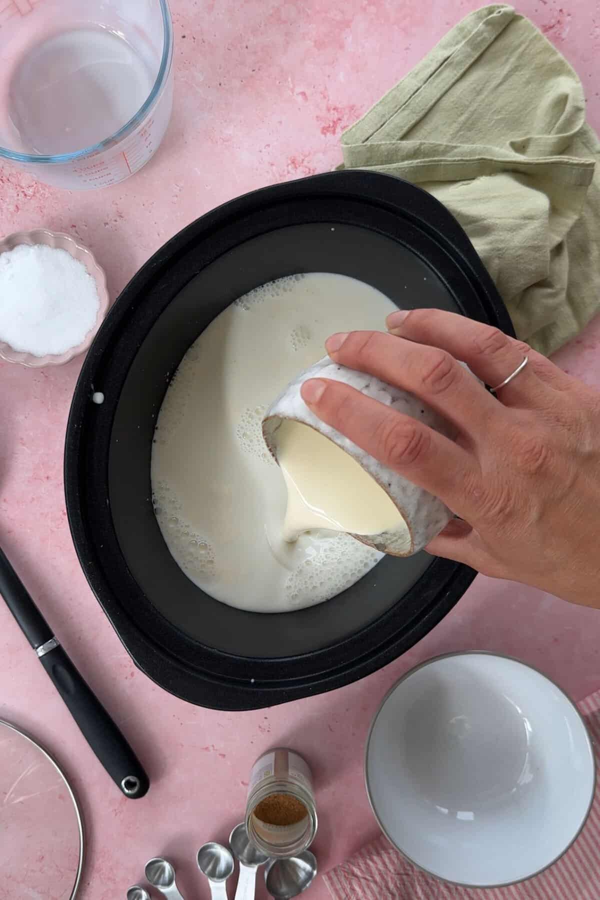 Process shot of slow cooker rice pudding showing the cream being poured into the slow cooker.