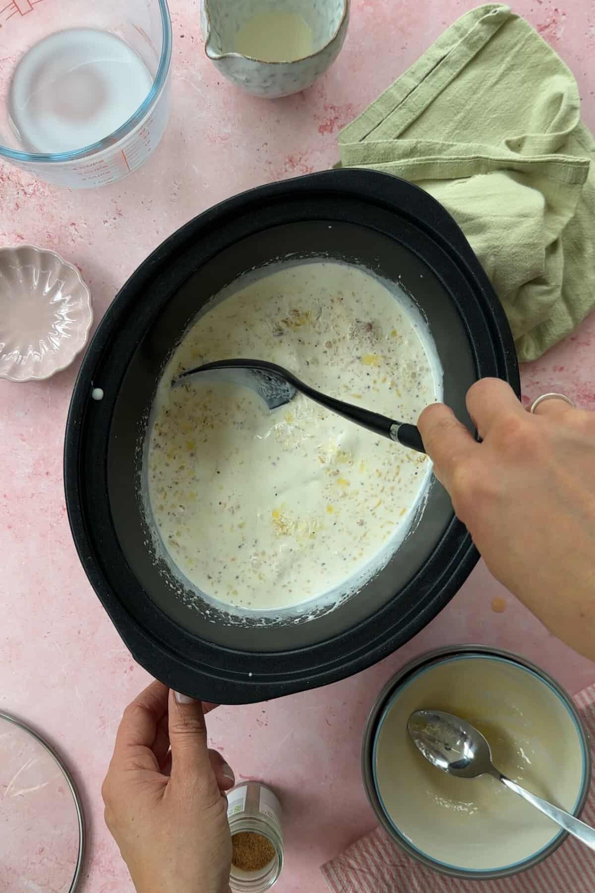 Process shot of slow cooker rice pudding showing a spoon stirring the pan.
